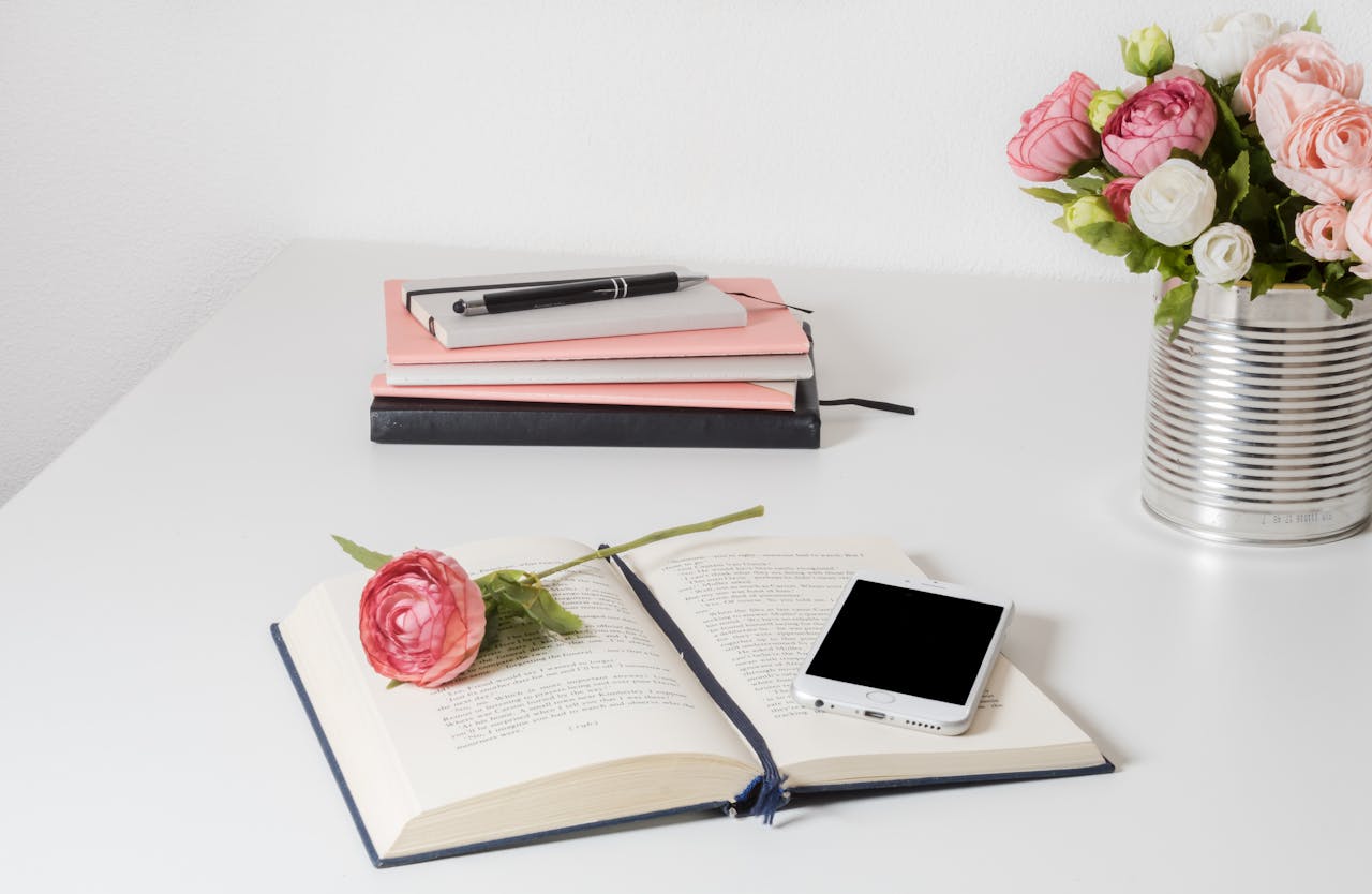 about-us A stylish home office setup with open book, smartphone, and flowers on a white desk.